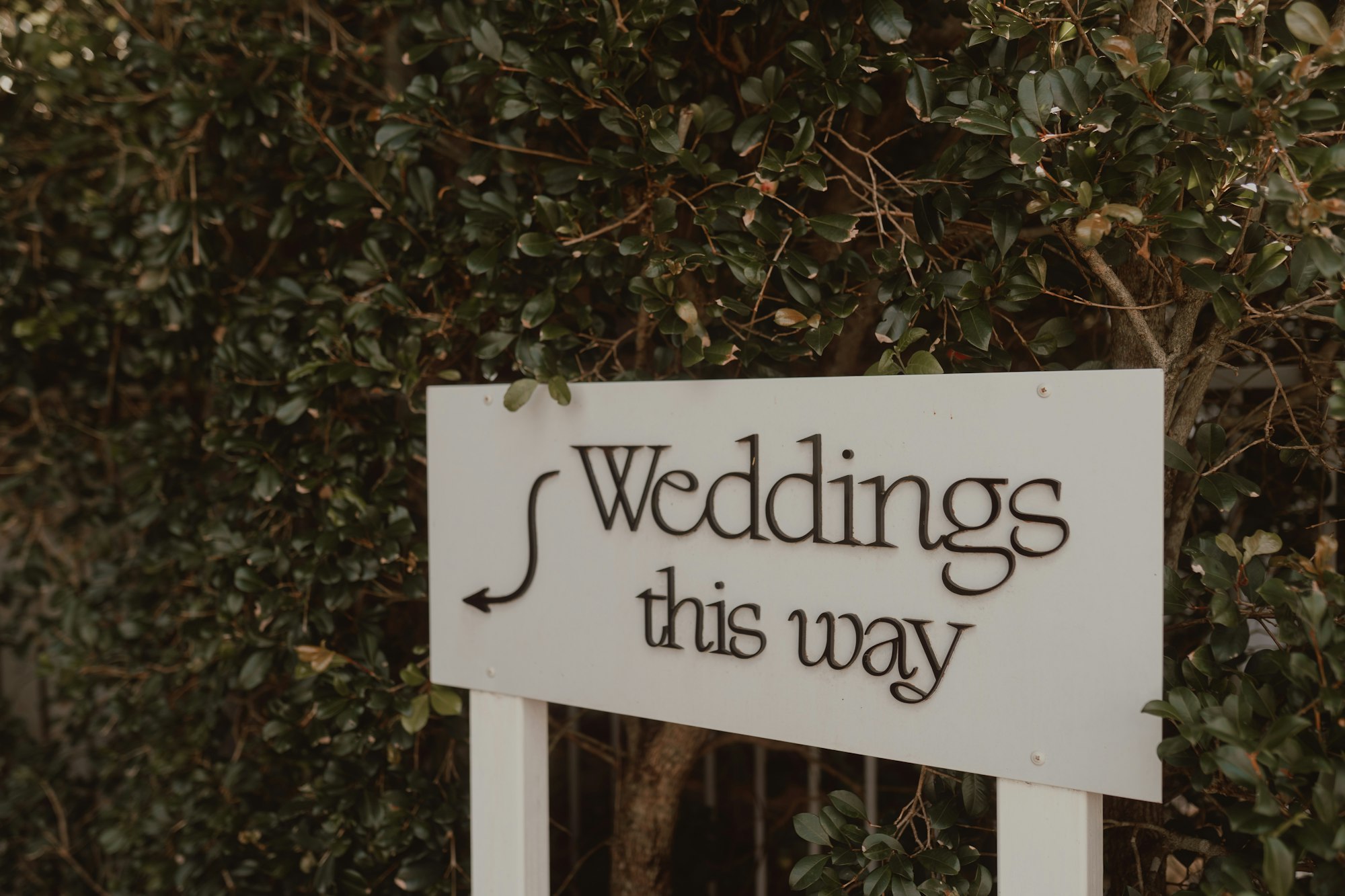 A white sign at a venue entrance reading weddings this way, with an arrow