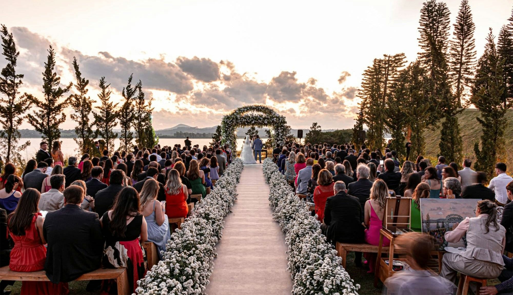 Guests seated in rows facing a lakeside wedding ceremony in progress on an open lawn