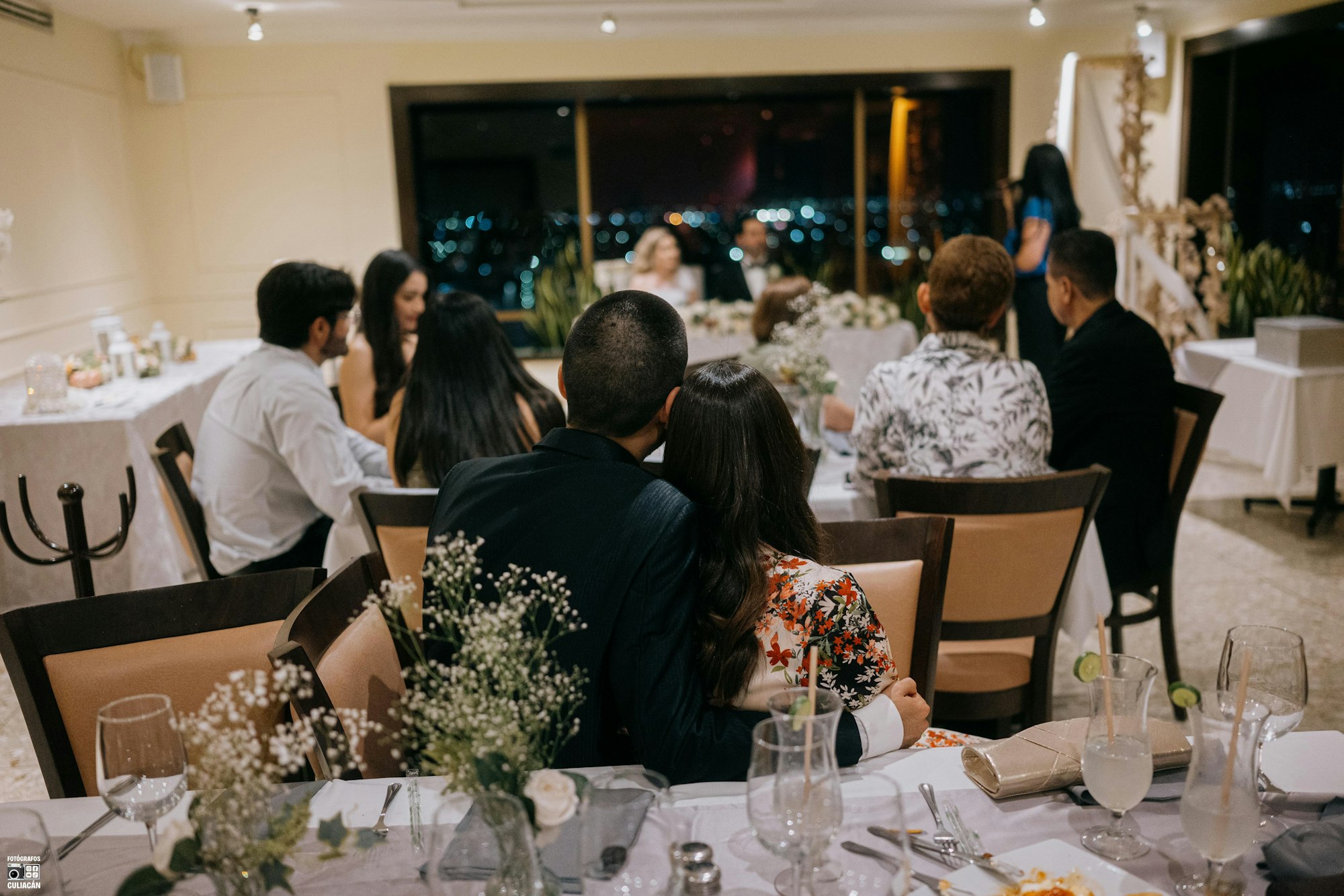 Guests seated at long candlelit tables under festoon lights at a night wedding reception