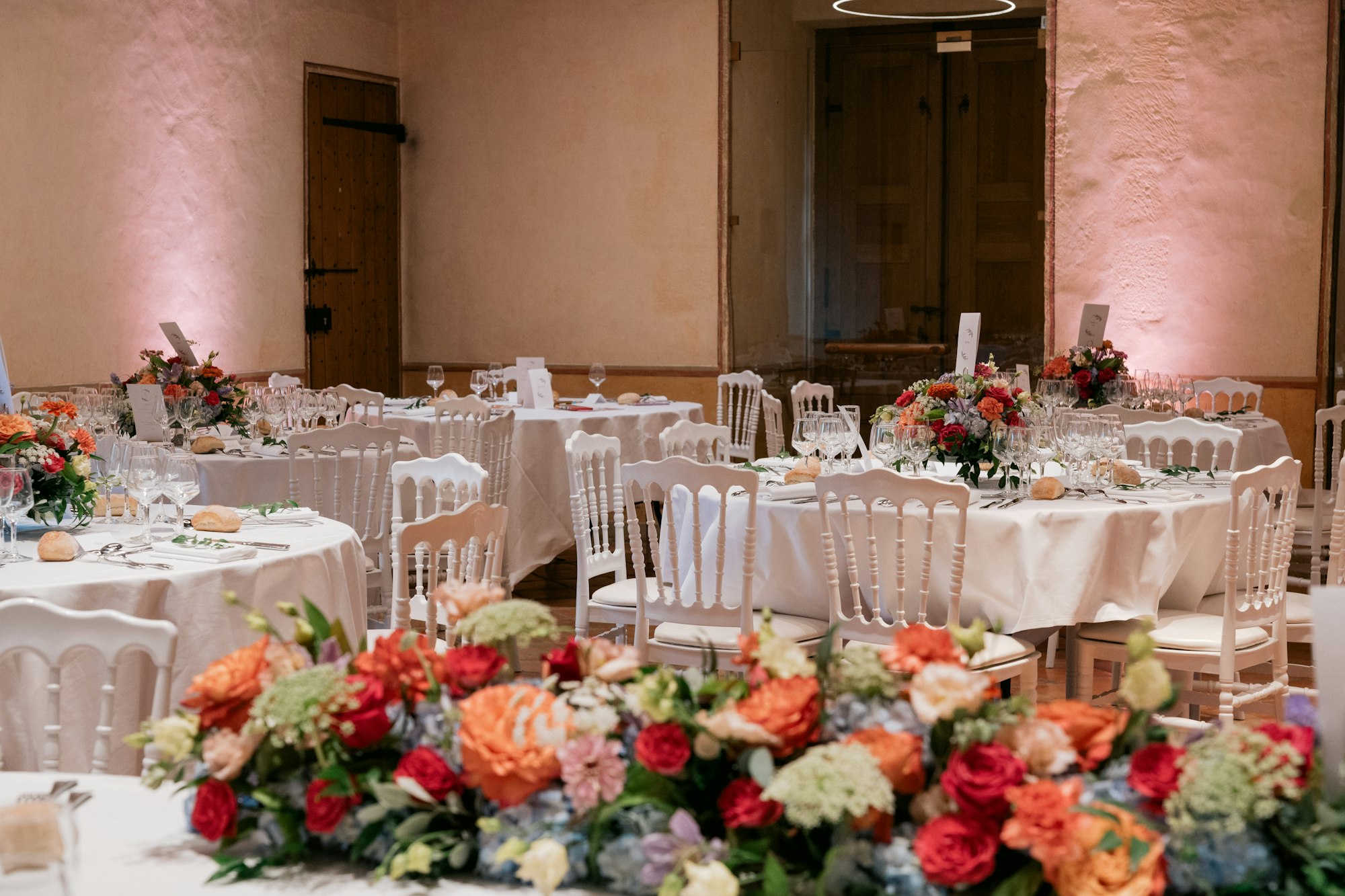 Round tables laid with glassware, bread rolls and orange and red centrepieces in a reception room that no guest has walked into yet