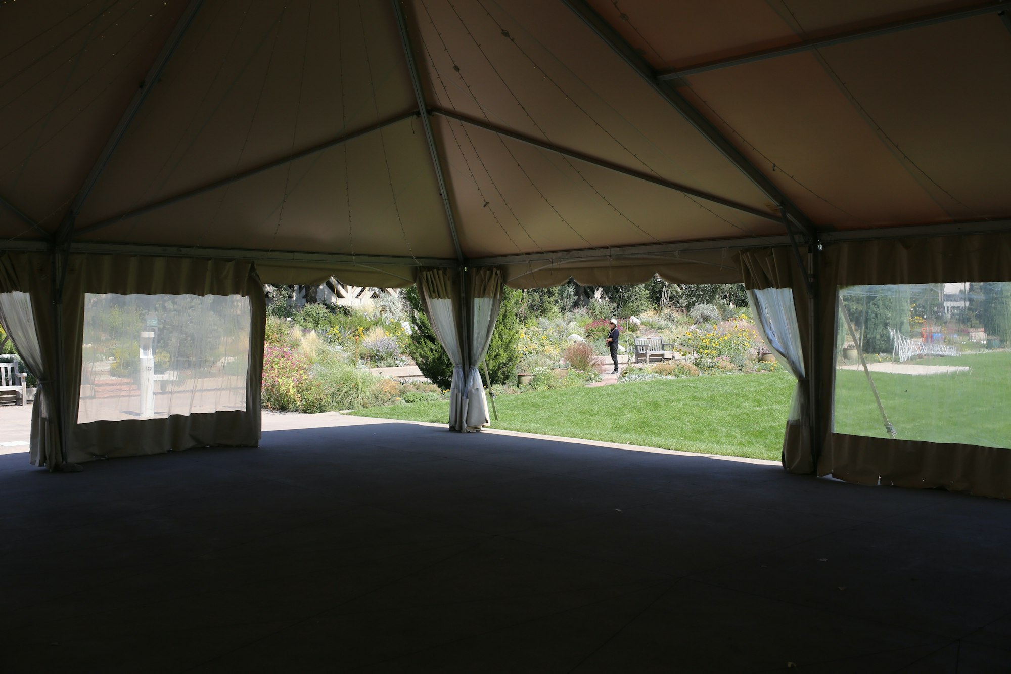 An empty garden marquee with the floor laid and the side curtains tied back, one person standing out on the path hours before guests arrive